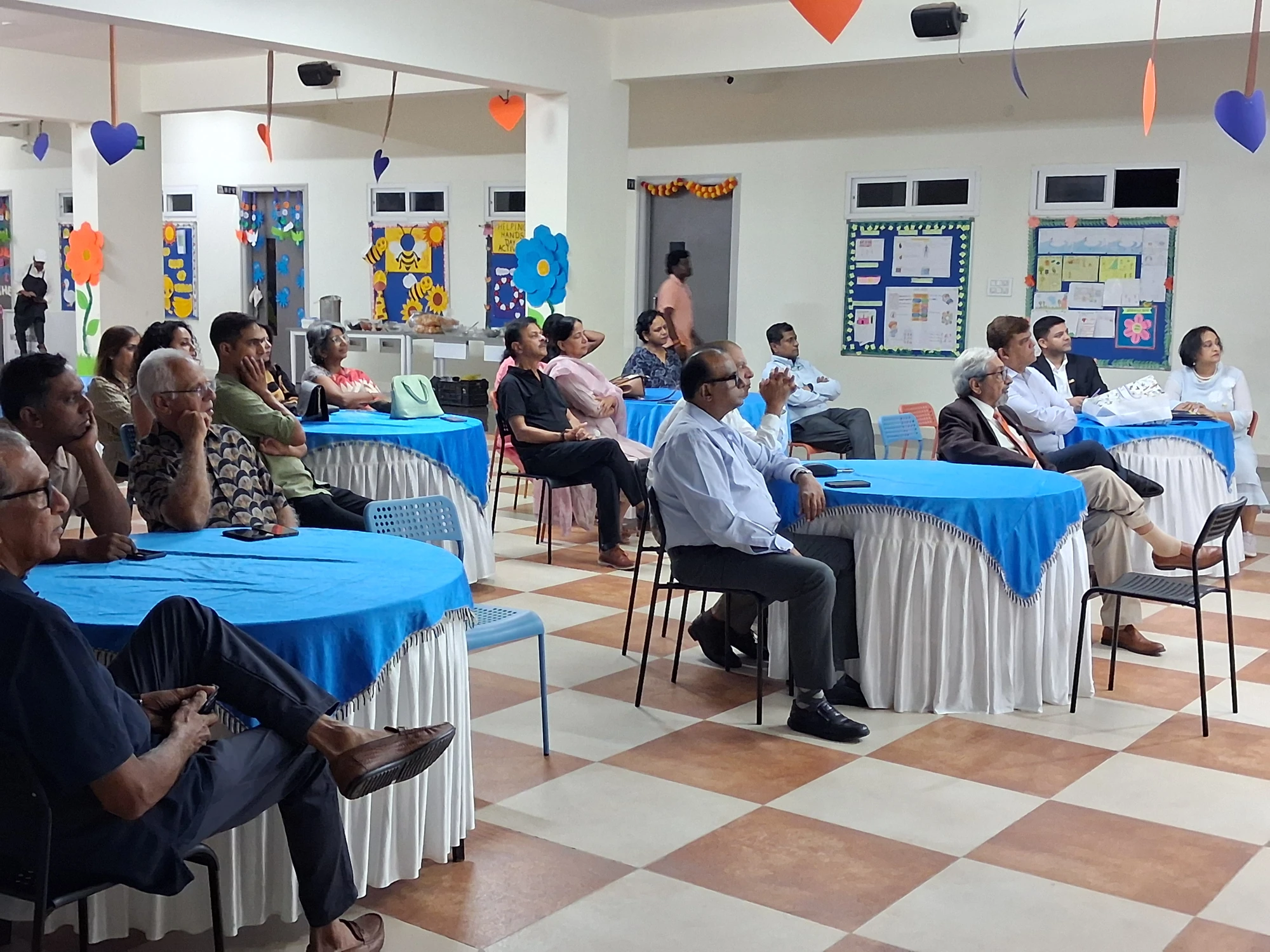 Members seated on chairs around blue-covered tables at the first club meeting